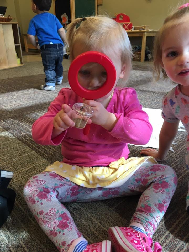 Child looking through a red magnifying glass at a small container