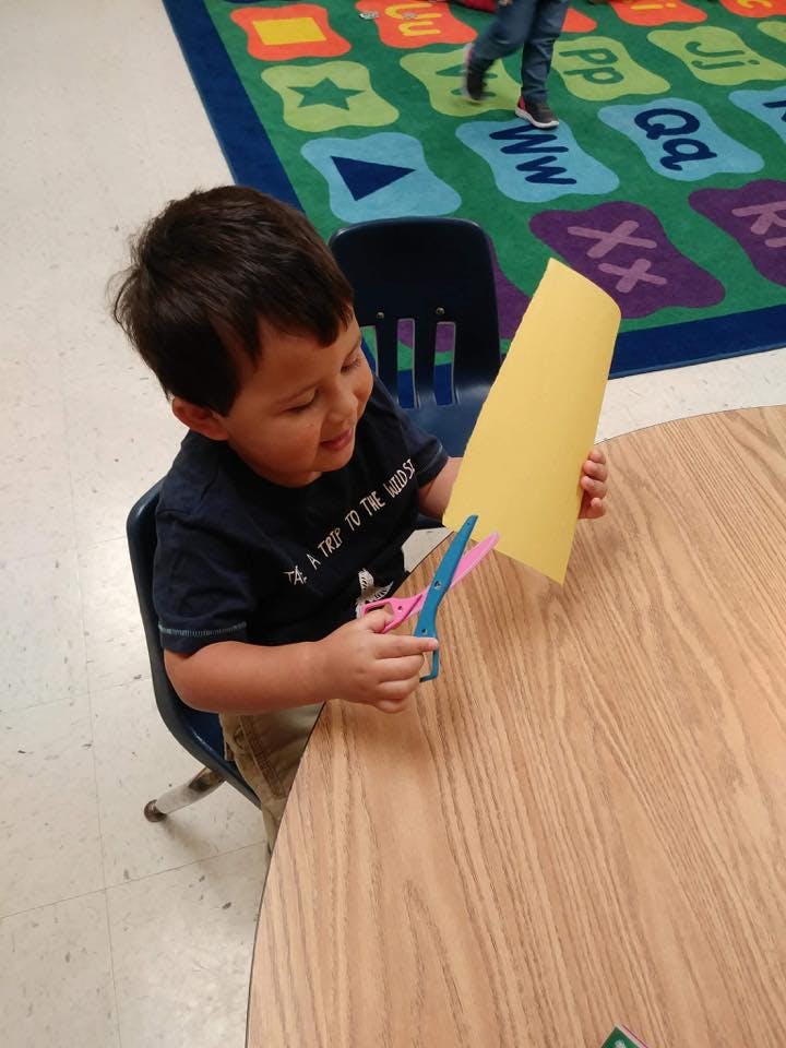 Child cutting yellow paper with scissors at a table