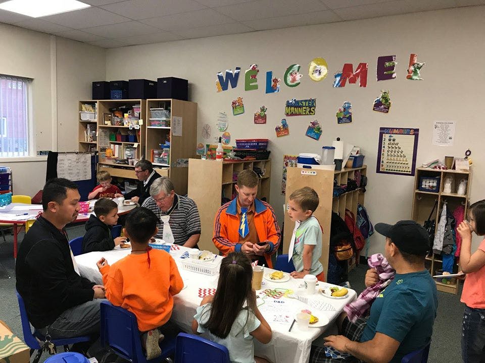 Adults and children sitting at tables in a classroom