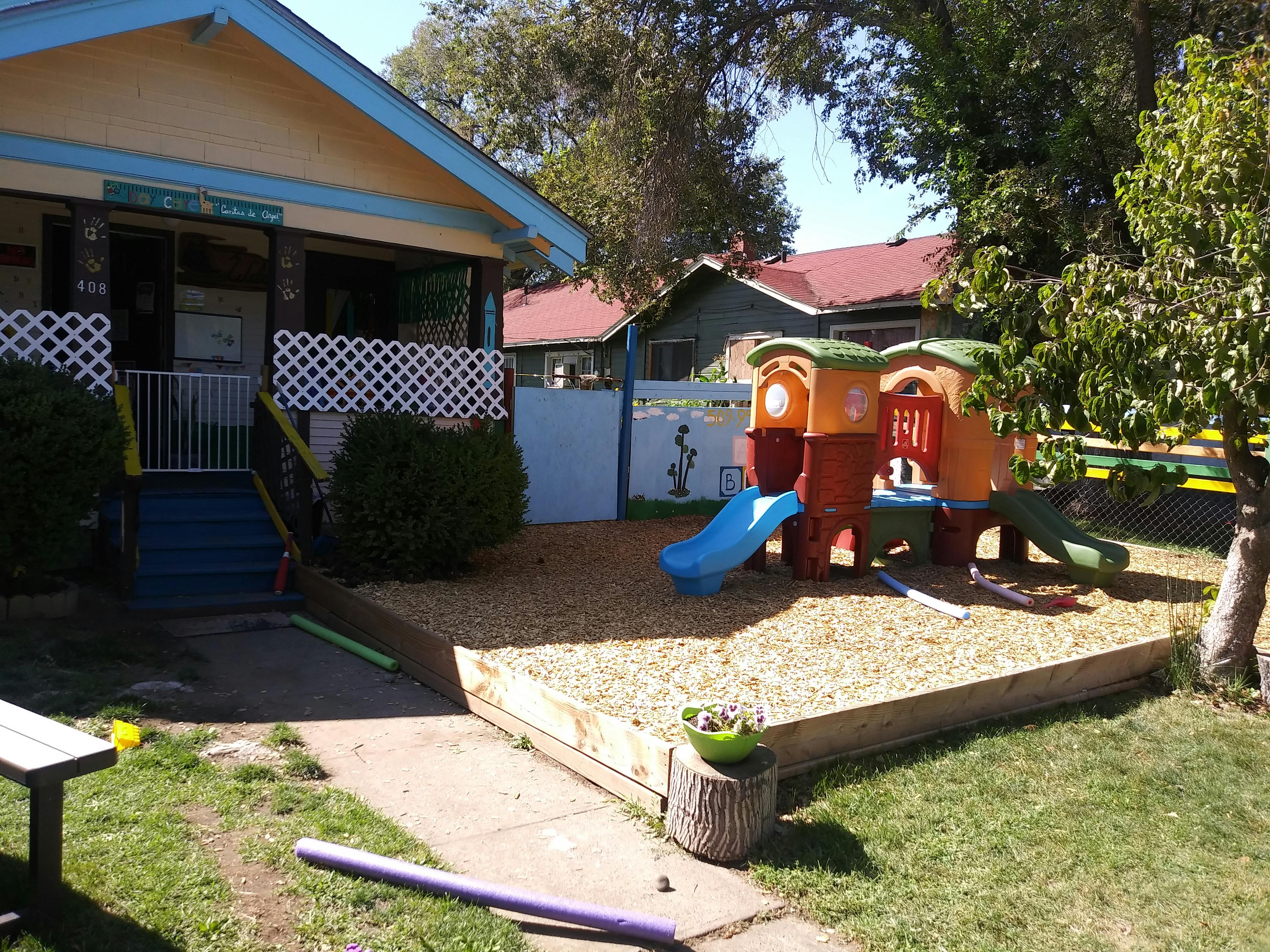 House with a porch next to a playground with a slide and wood chips