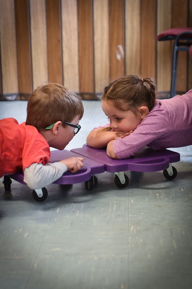 Two children lying on purple scooters facing each other