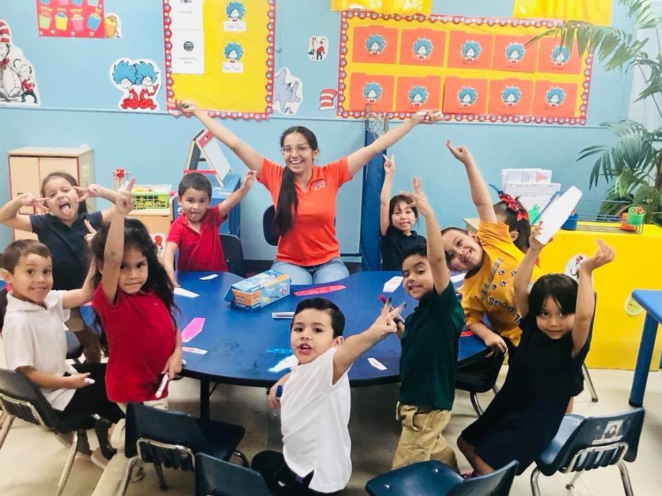 Adult and children in a classroom raising their arms