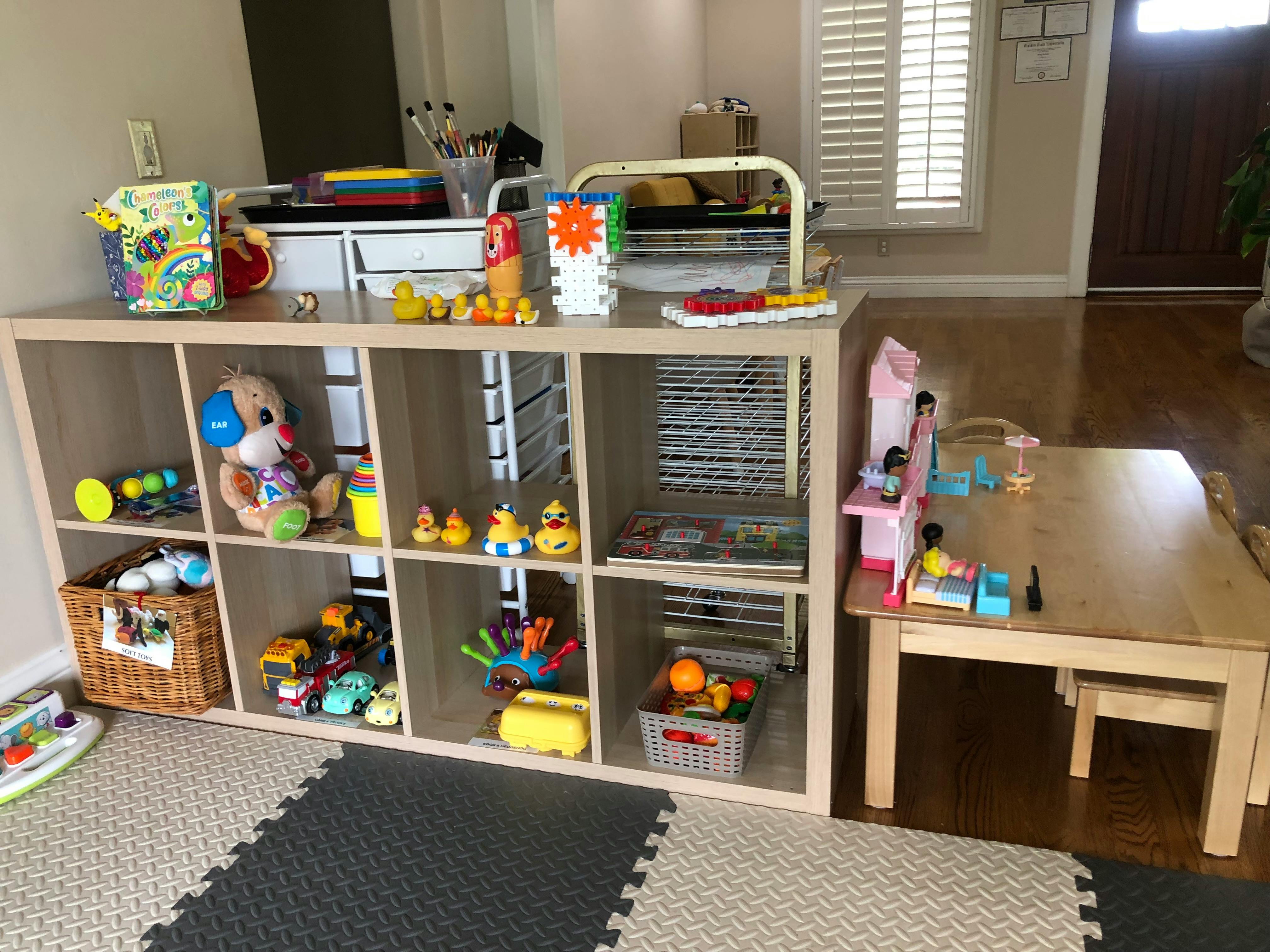 Shelving unit filled with toys next to a small wooden table and chairs