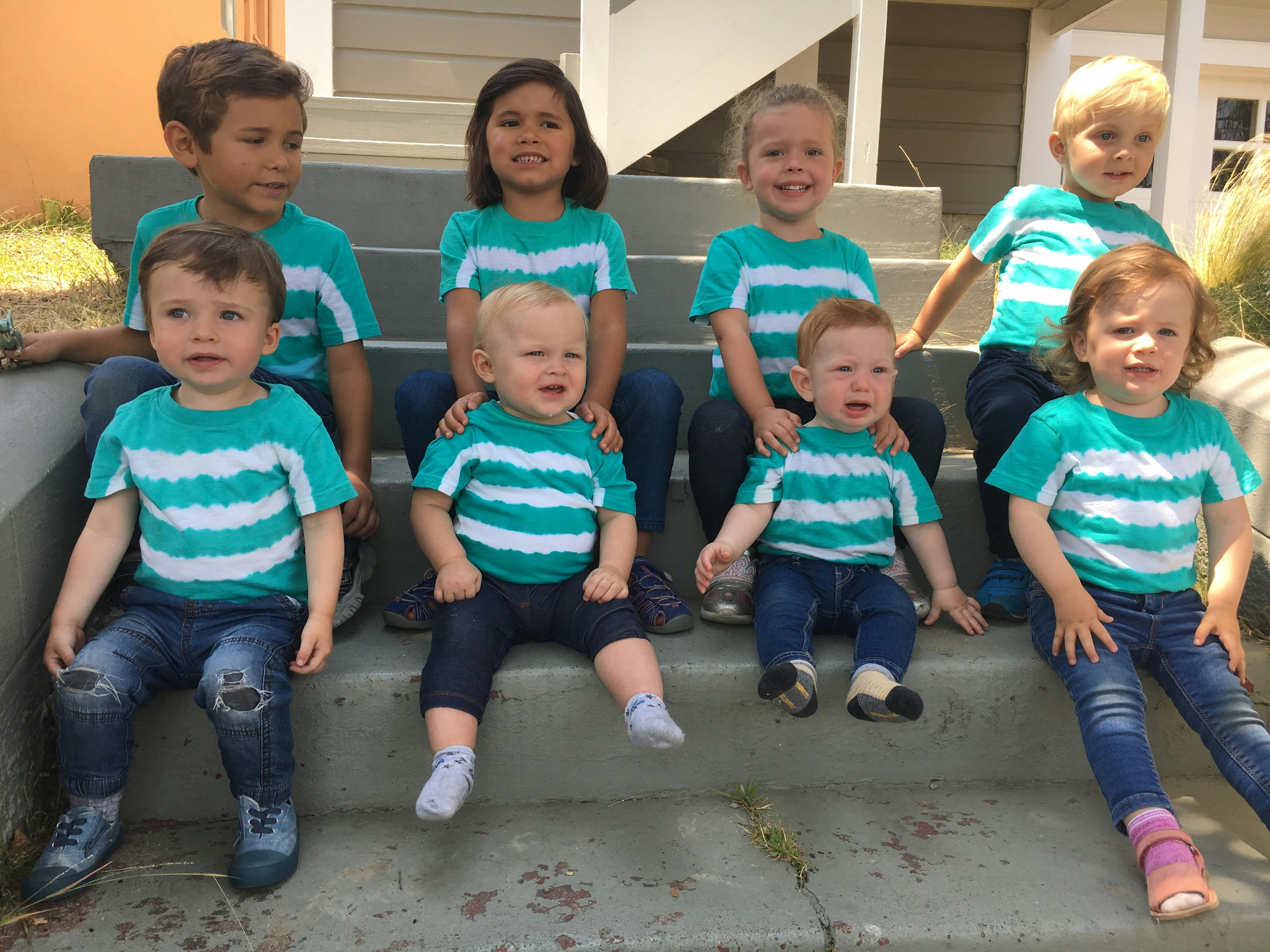 Group of seven children and toddlers in matching striped shirts sitting on concrete steps