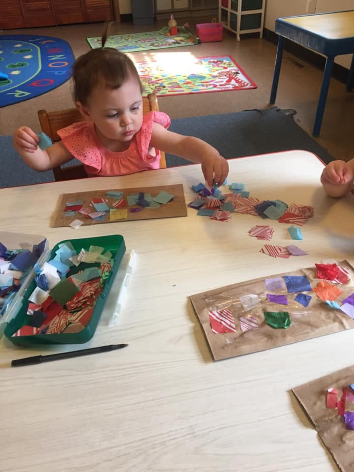 Child sitting at a table doing a craft with colorful paper pieces