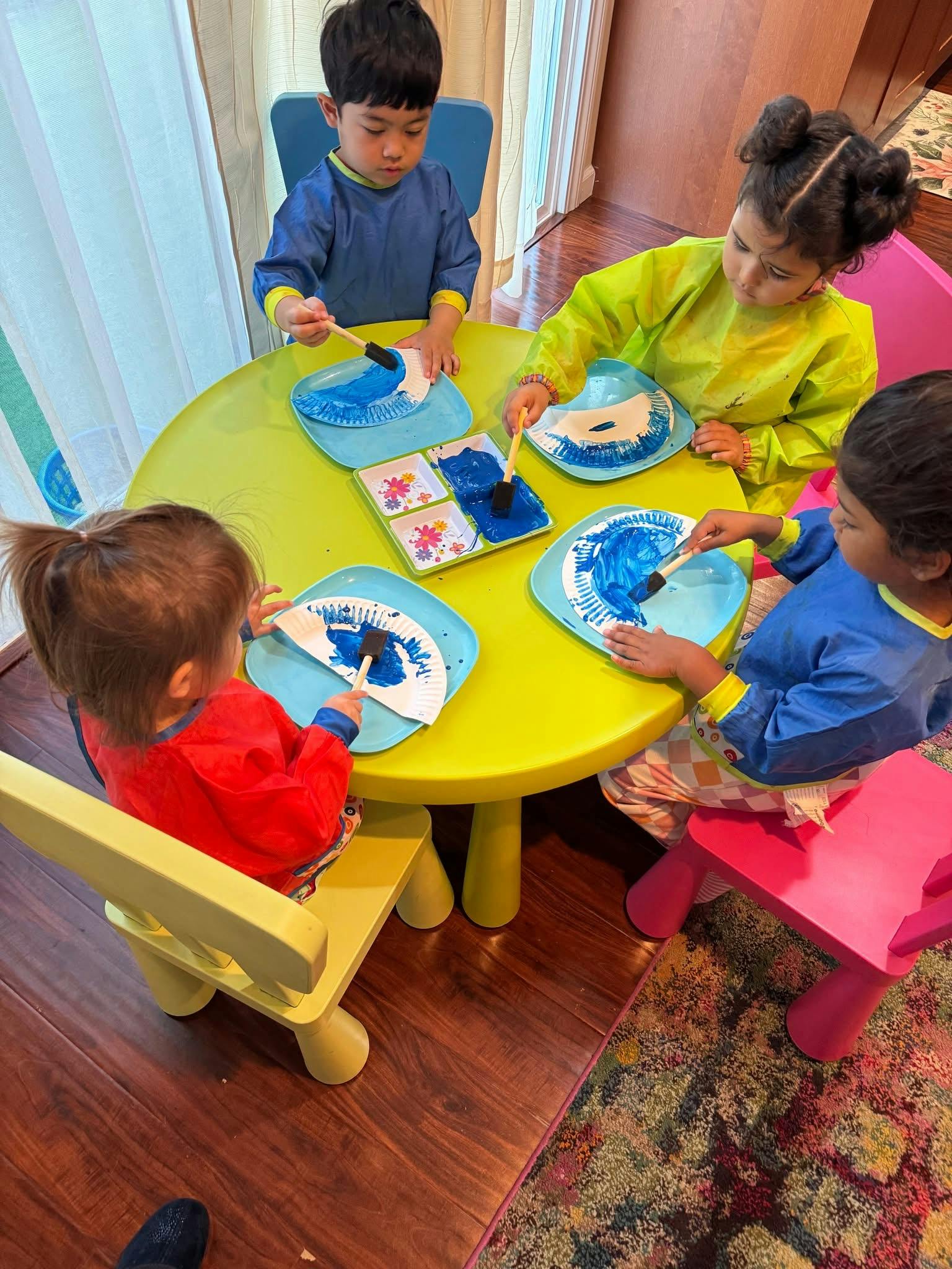 Four children painting paper plates at a table