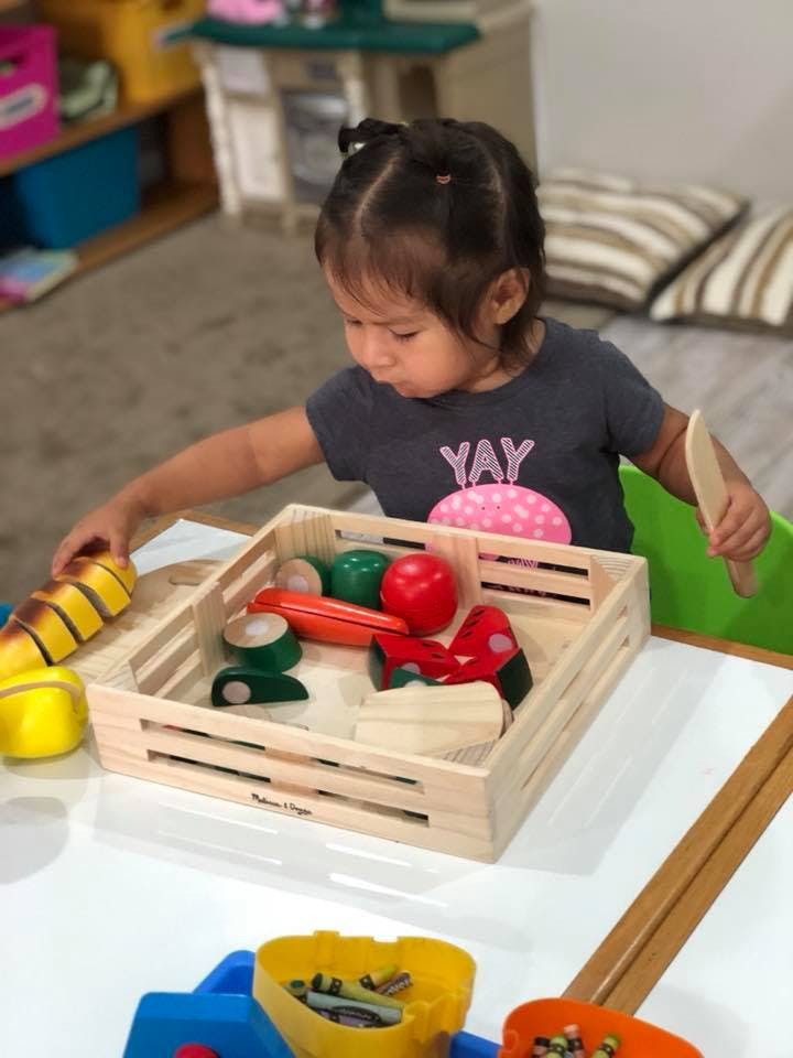 Child playing with wooden toy food in a crate