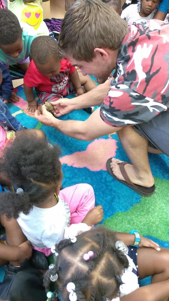 Person showing a small animal to children on a colorful rug