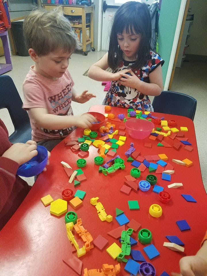 Two children playing with colorful building blocks on a red table
