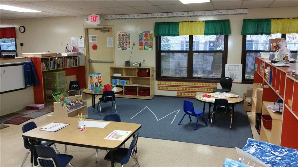 Empty classroom with small tables and chairs, shelves with books and supplies