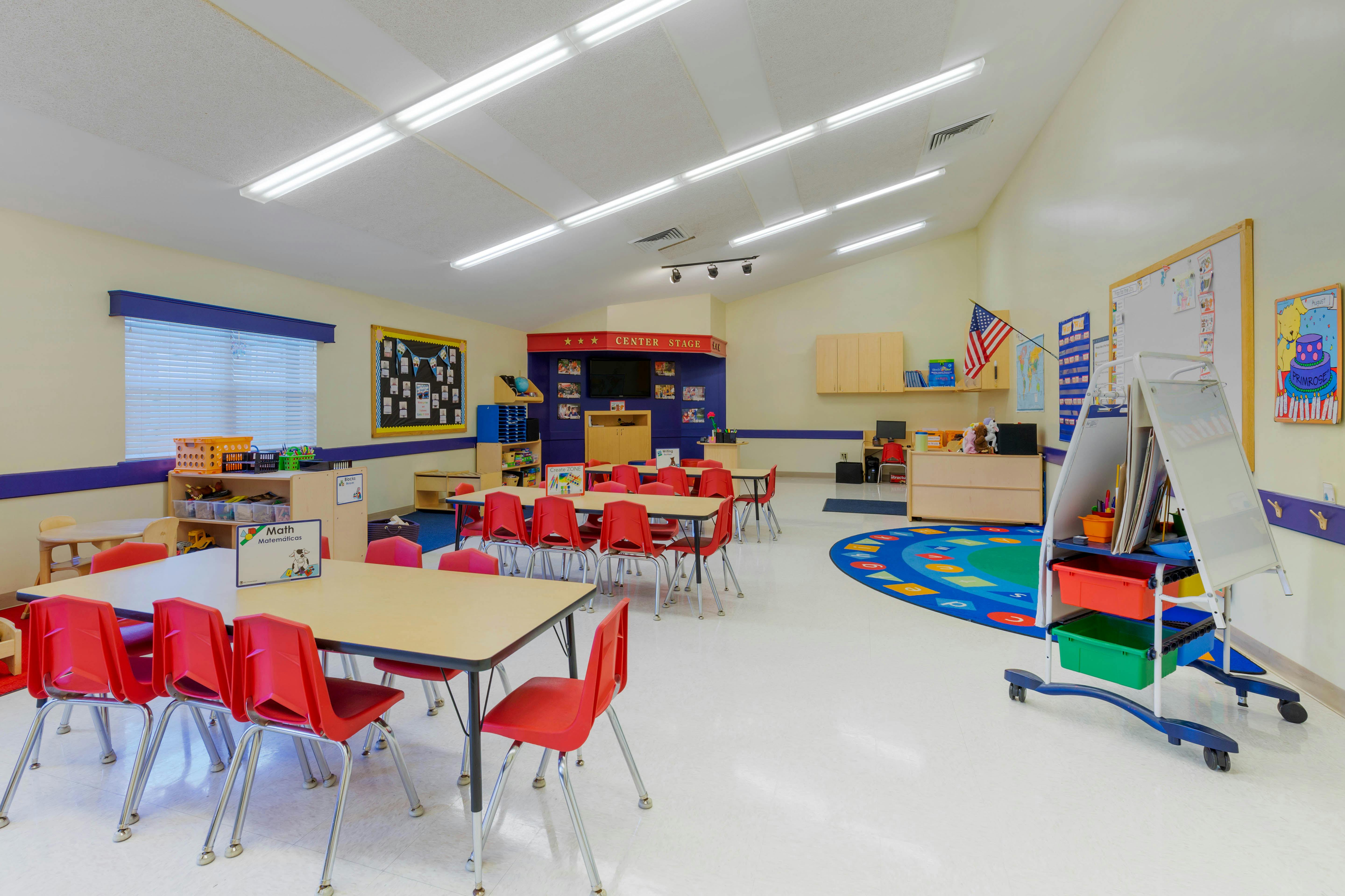 Empty classroom with small tables and red chairs, a blue and green rug