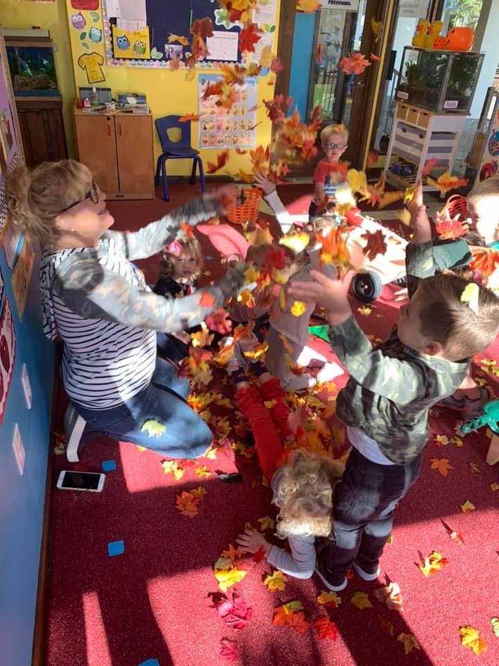 Person and children playing with autumn leaves in a classroom