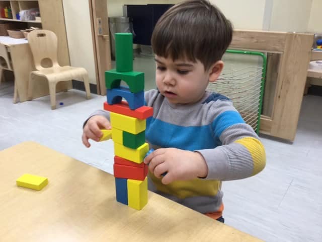 Child stacking colorful blocks on a table in a classroom