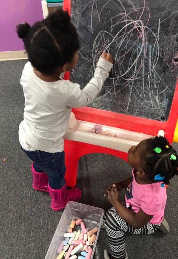 Child drawing on a chalkboard while another child watches
