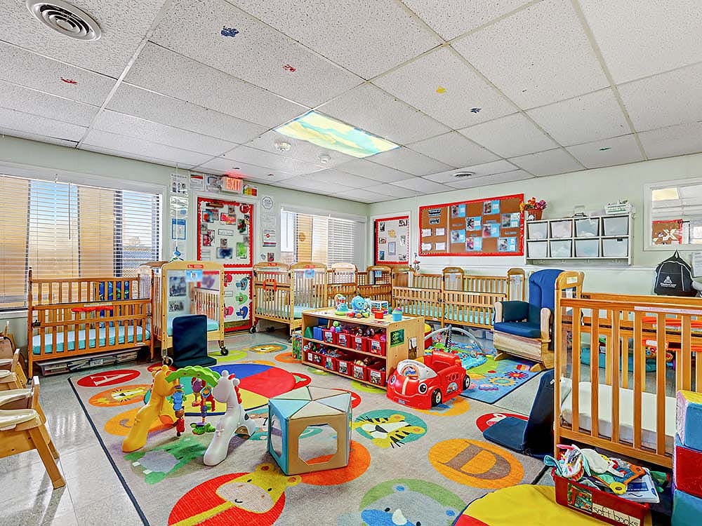 daycare classroom with multiple wooden cribs, toys on a colorful animal rug