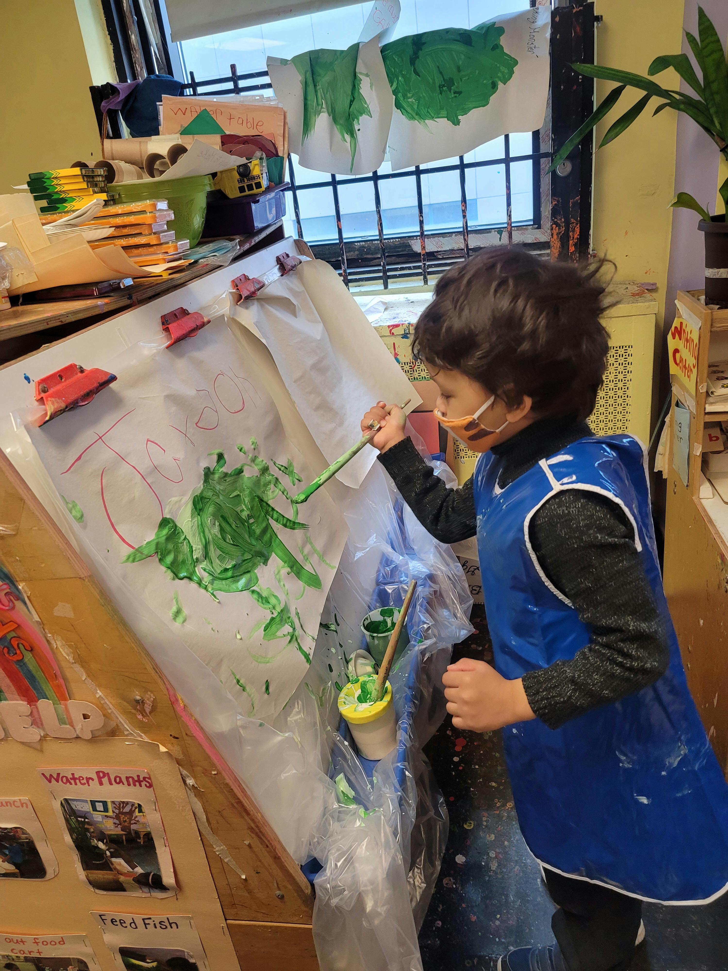 Child in an art smock painting on an easel