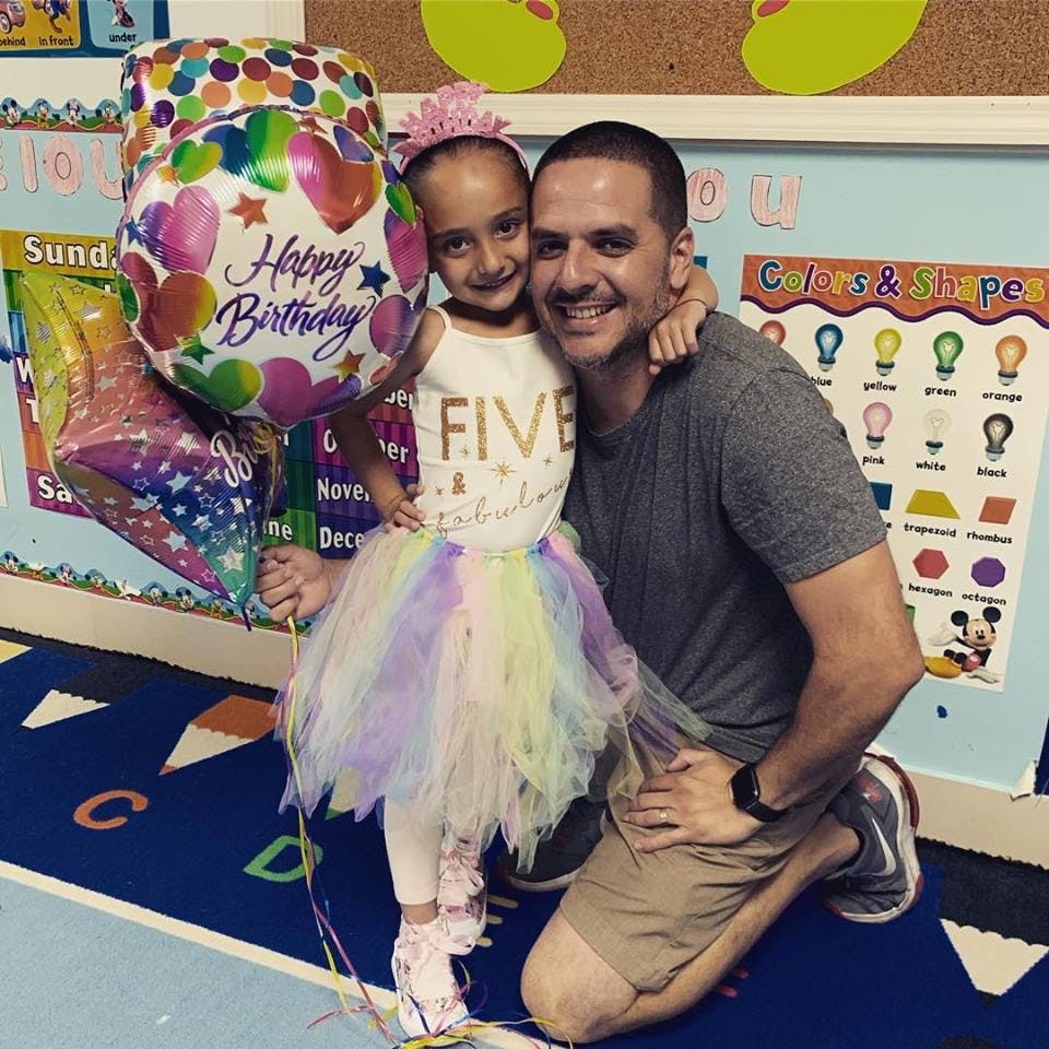 Person kneeling next to a child holding a Happy Birthday balloon