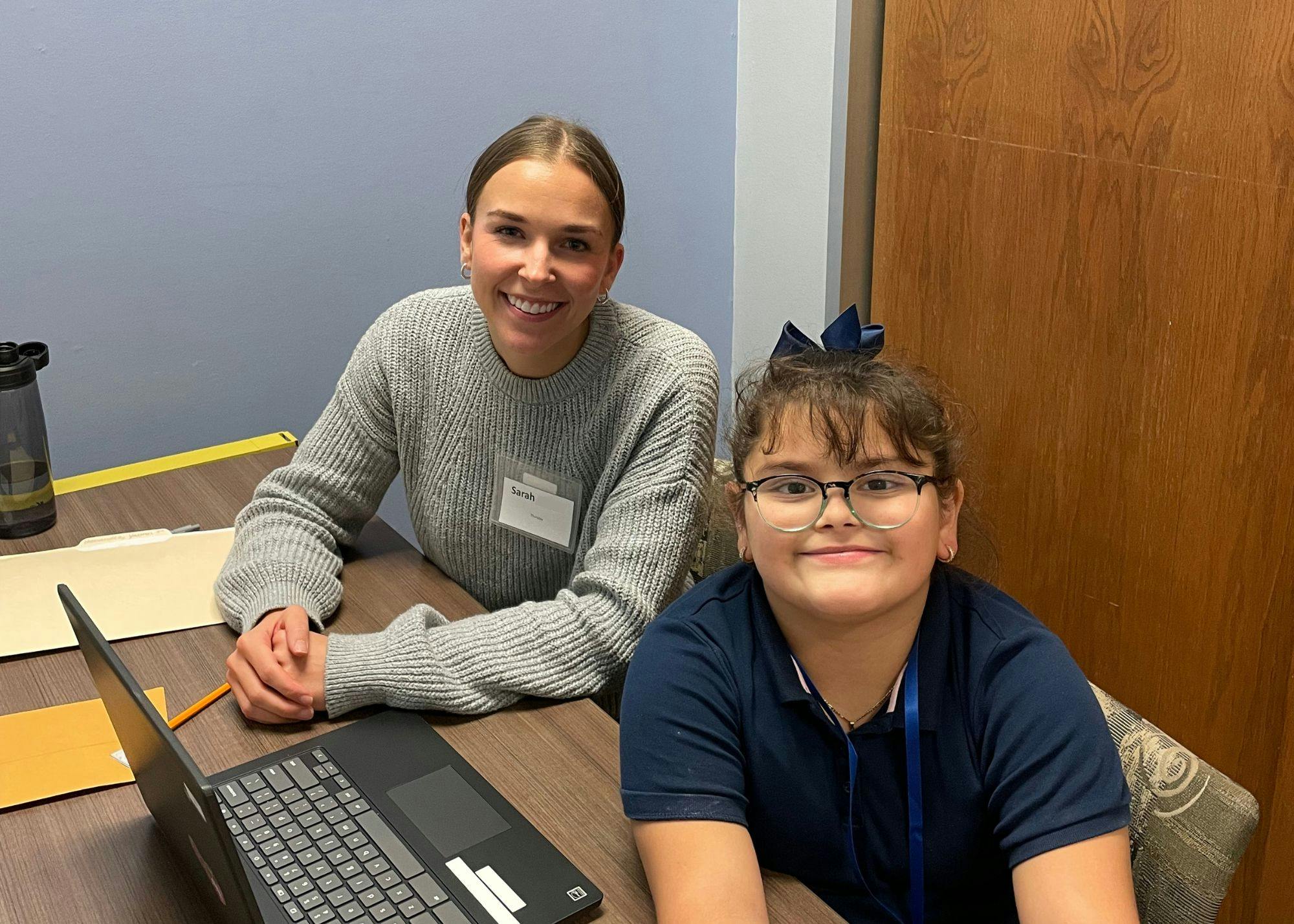 Person and child sitting at a desk with a laptop