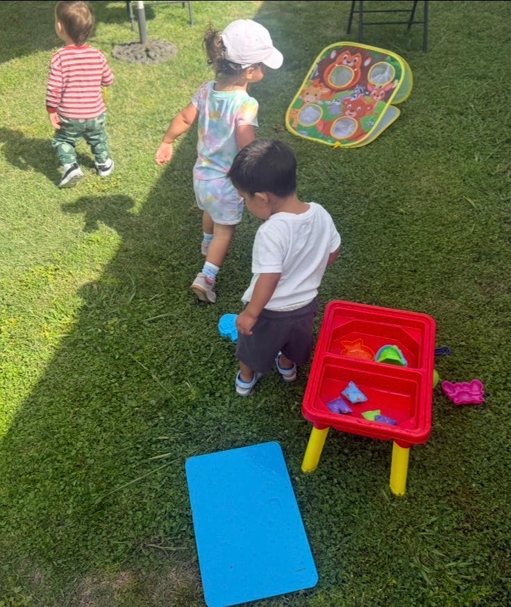 Three children playing outdoors on grass with various toys