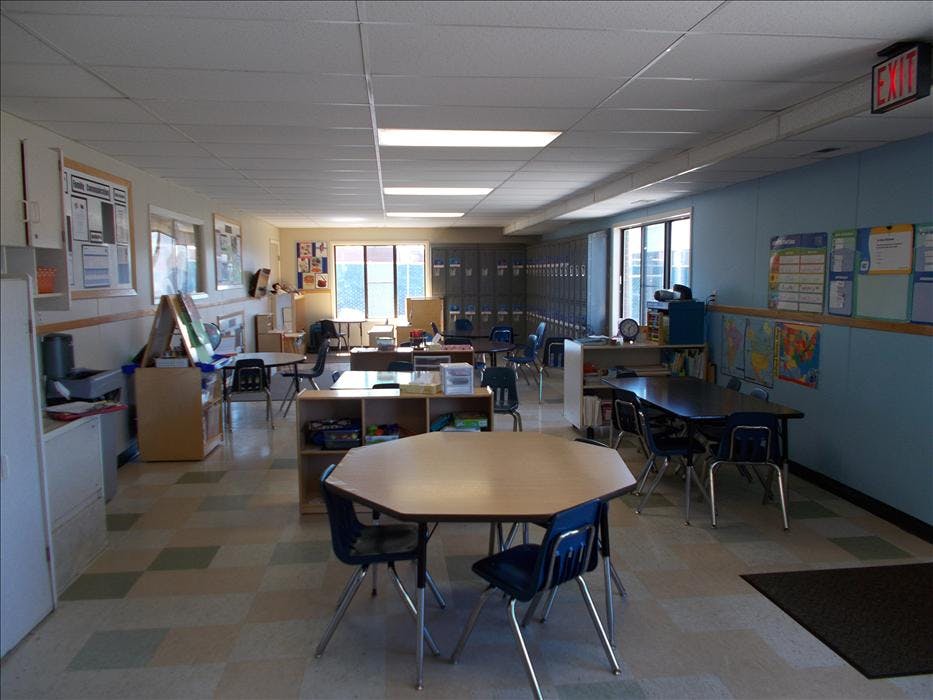 Empty classroom with multiple tables, chairs, and cubbies