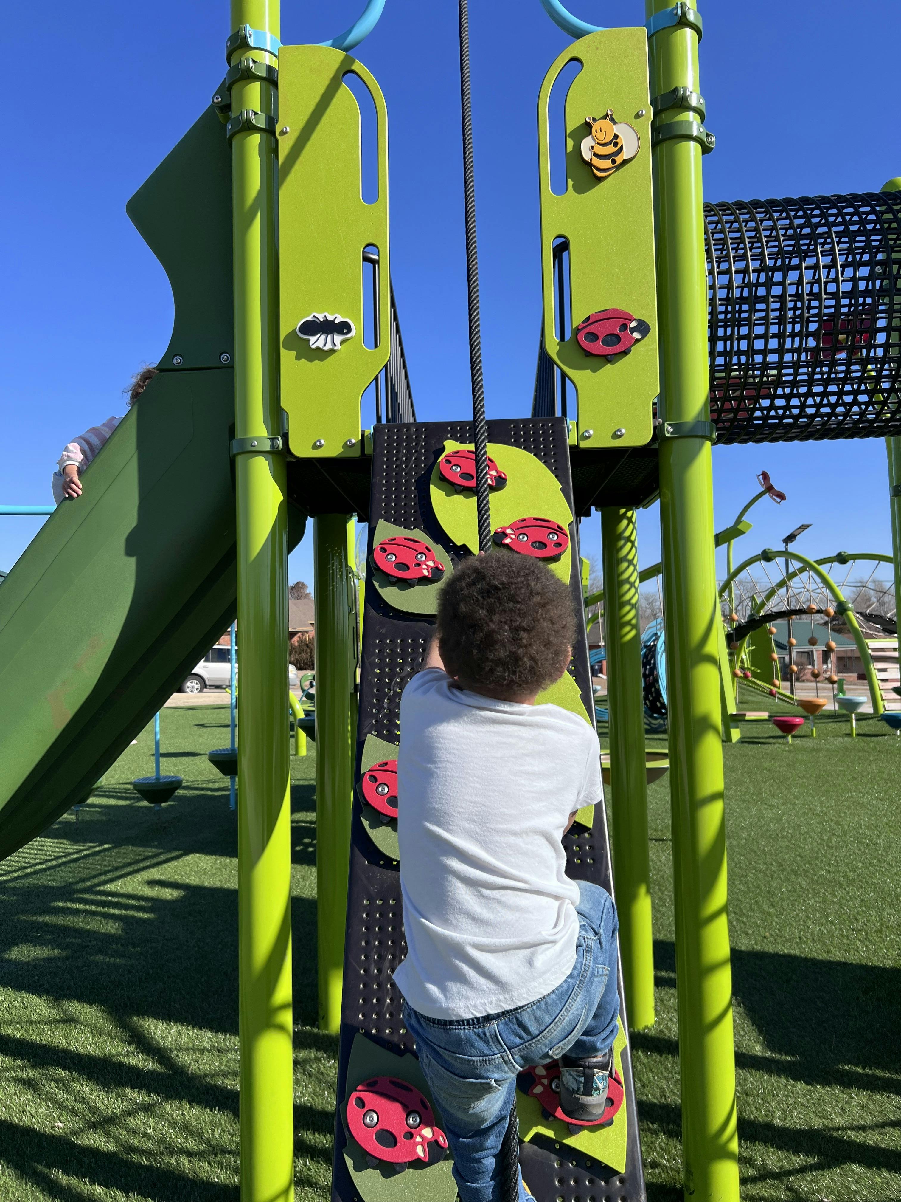 Child climbing playground structure with ladybug-shaped holds