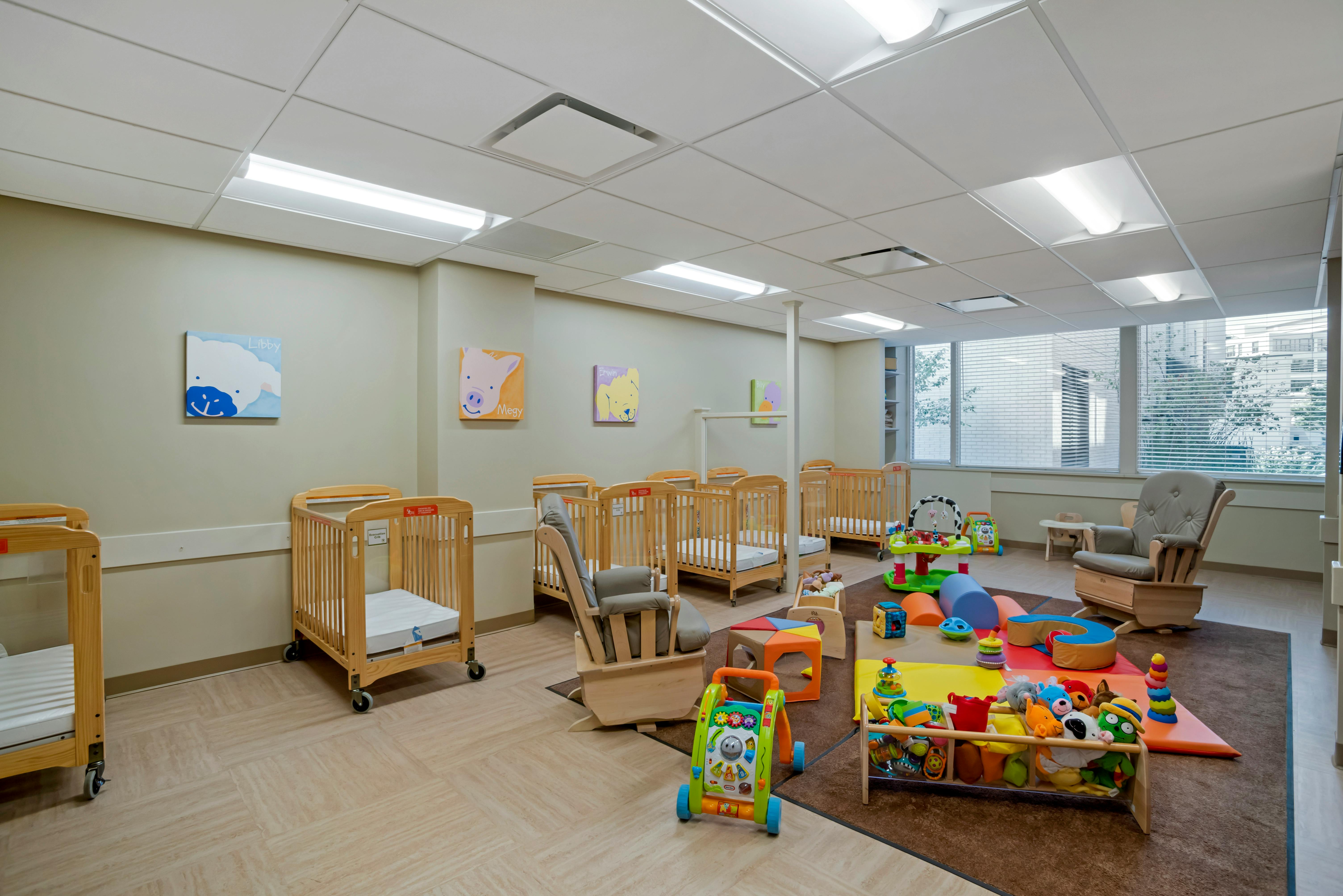 A room with several wooden cribs, a rocking chair, and colorful baby toys on a rug
