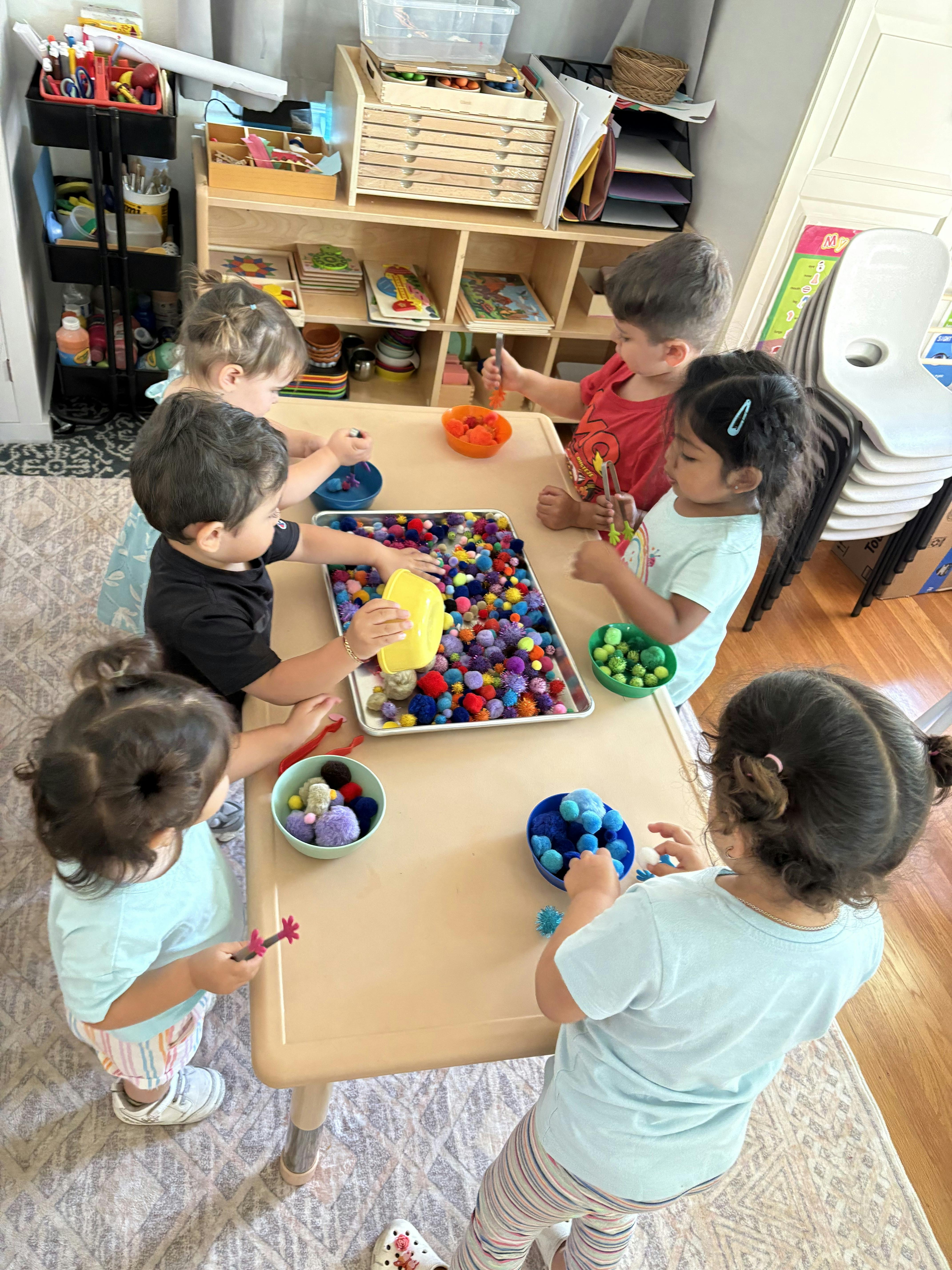 Children playing with colorful pom-poms at a table