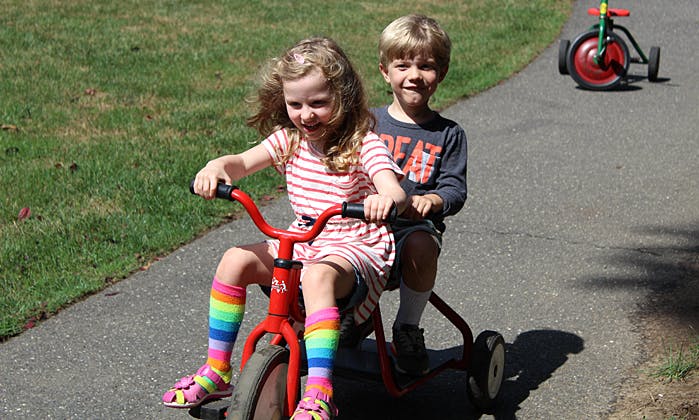 Two children riding a tricycle on a paved path