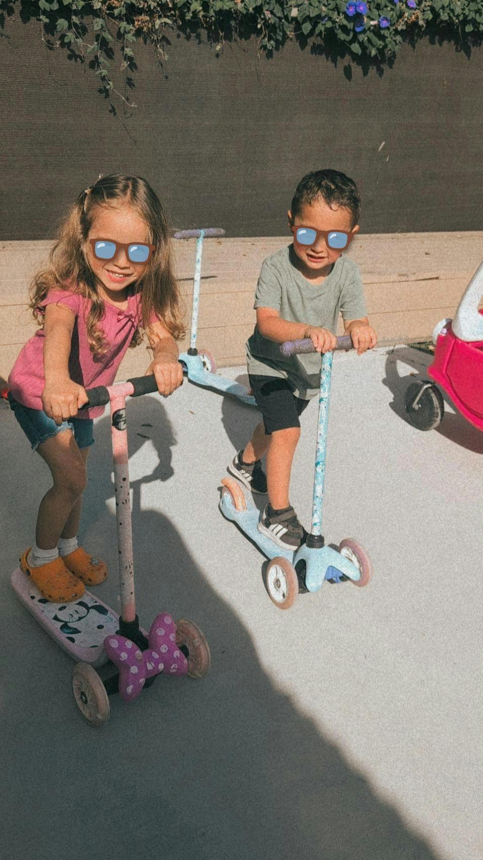 Two children riding scooters outside