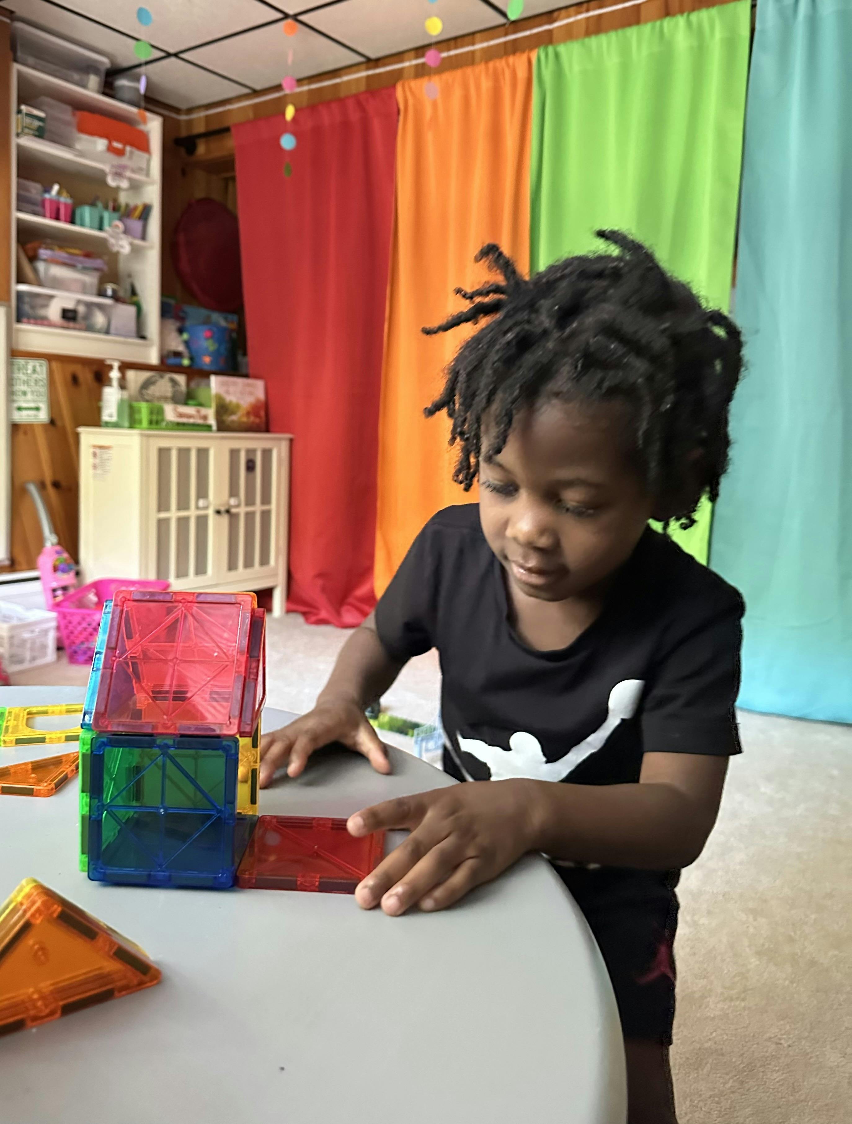 Child playing with colorful magnetic building tiles on a table