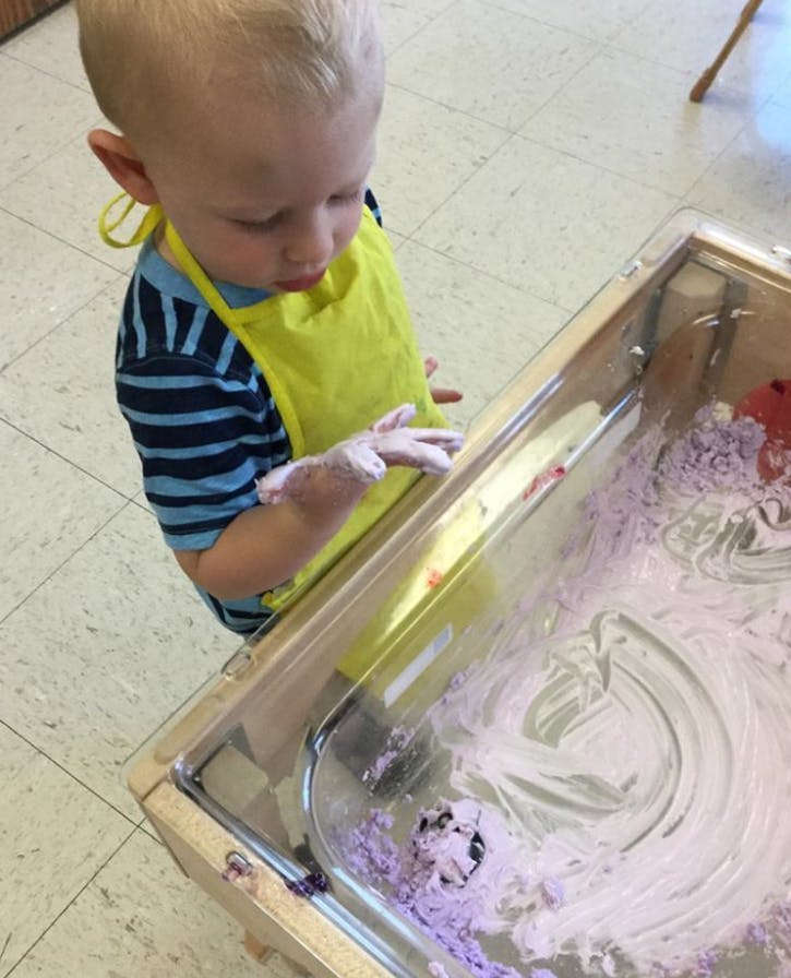 Child in yellow apron playing with purple foam in a sensory bin