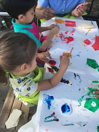 Two children painting at a table with an adult