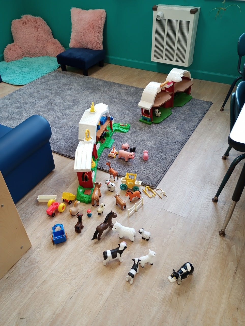 Toy farm animals and buildings on a rug and wooden floor