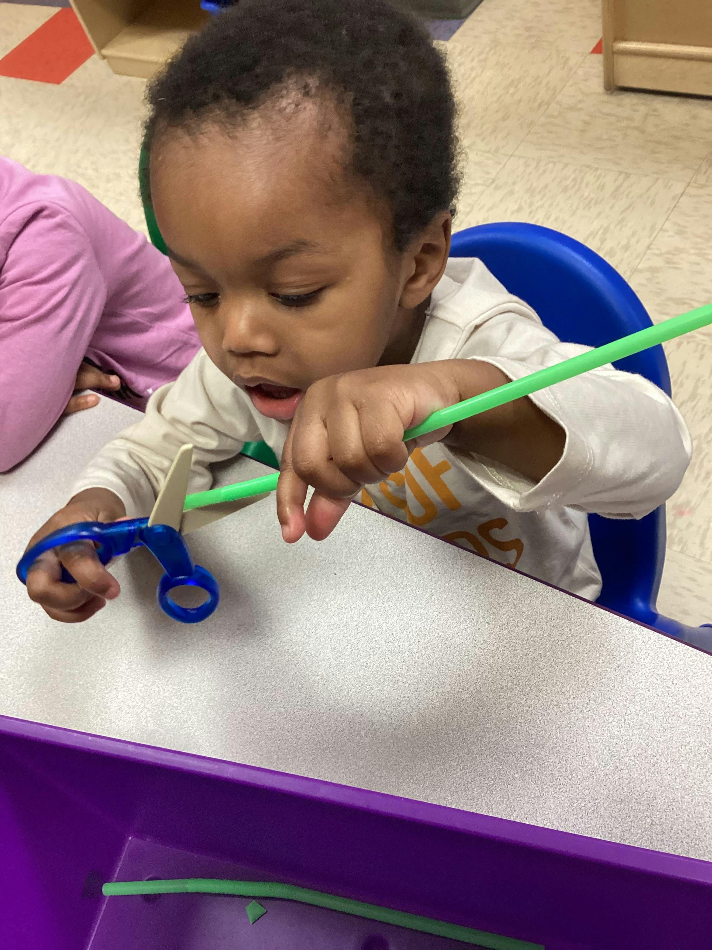 Child cutting a green pipe cleaner with blue scissors