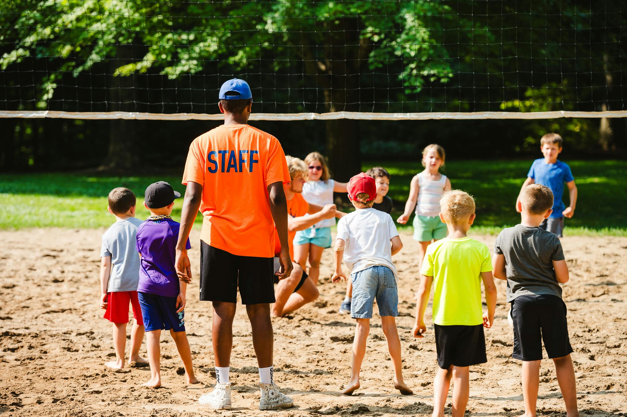 Person in "STAFF" shirt watching children play volleyball