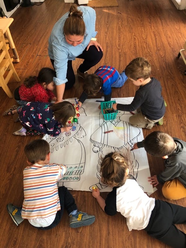 Adult and several children kneeling around a large coloring page on the floor