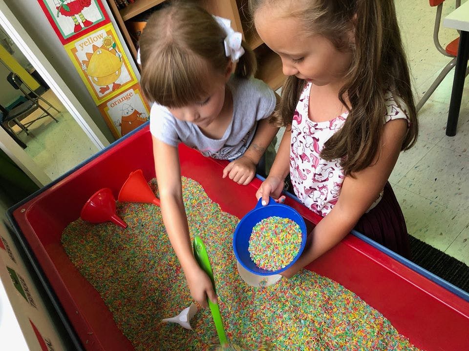 Two children playing with colorful sprinkles in a red bin