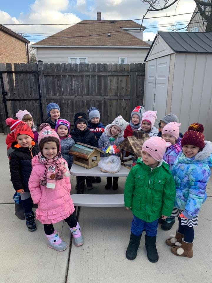 Group of children in winter hats and coats gathered around a table outdoors