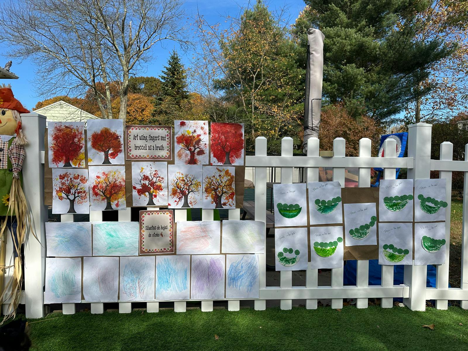 Children's artwork displayed on a white picket fence