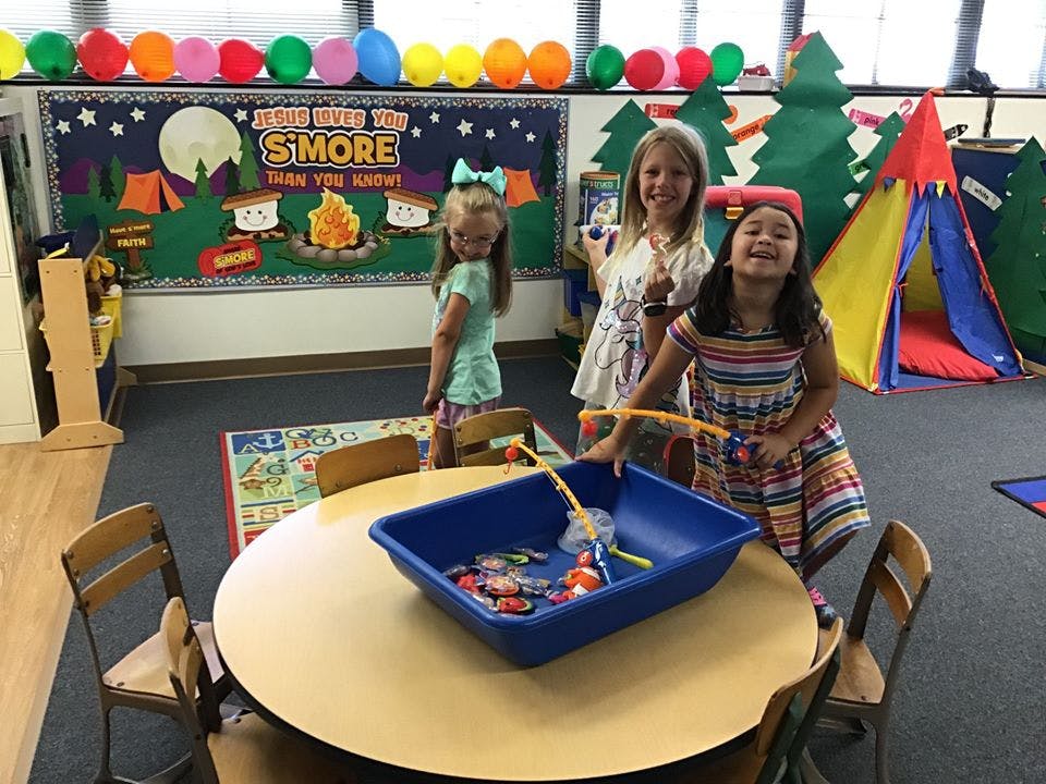 Three children playing with a fishing toy in a classroom