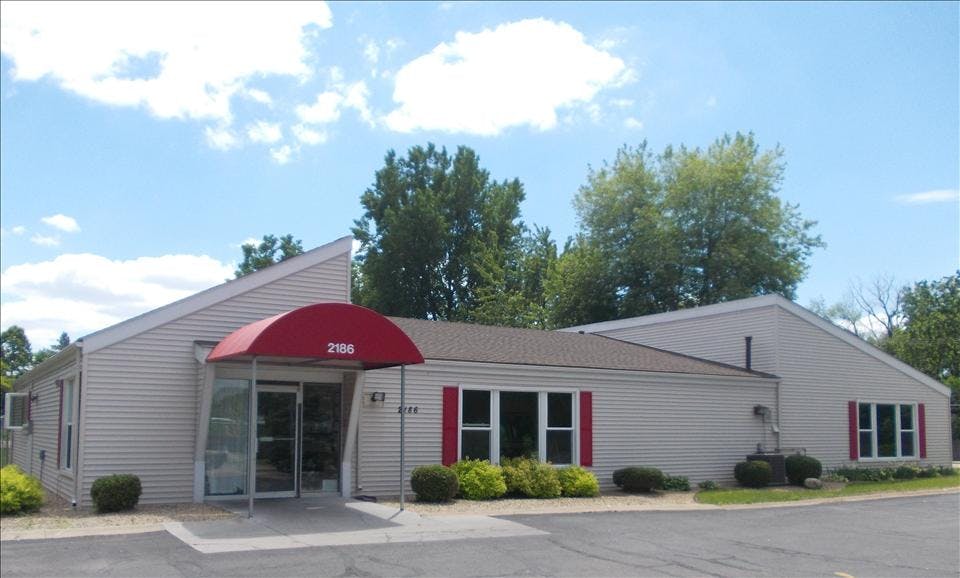 Single story building with beige siding, red awning, and red window shutters