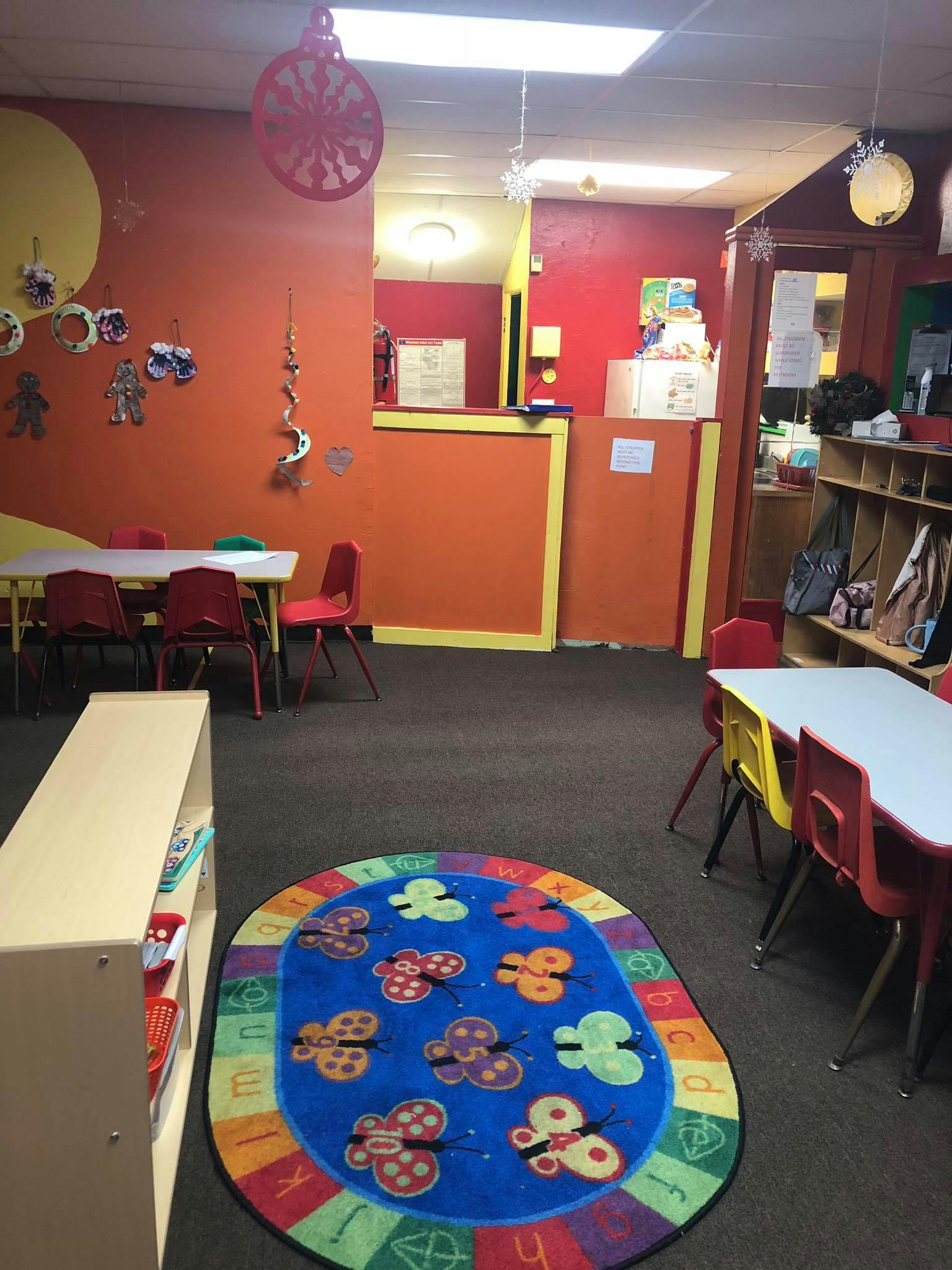 Classroom with small tables and chairs, a butterfly rug, and orange walls