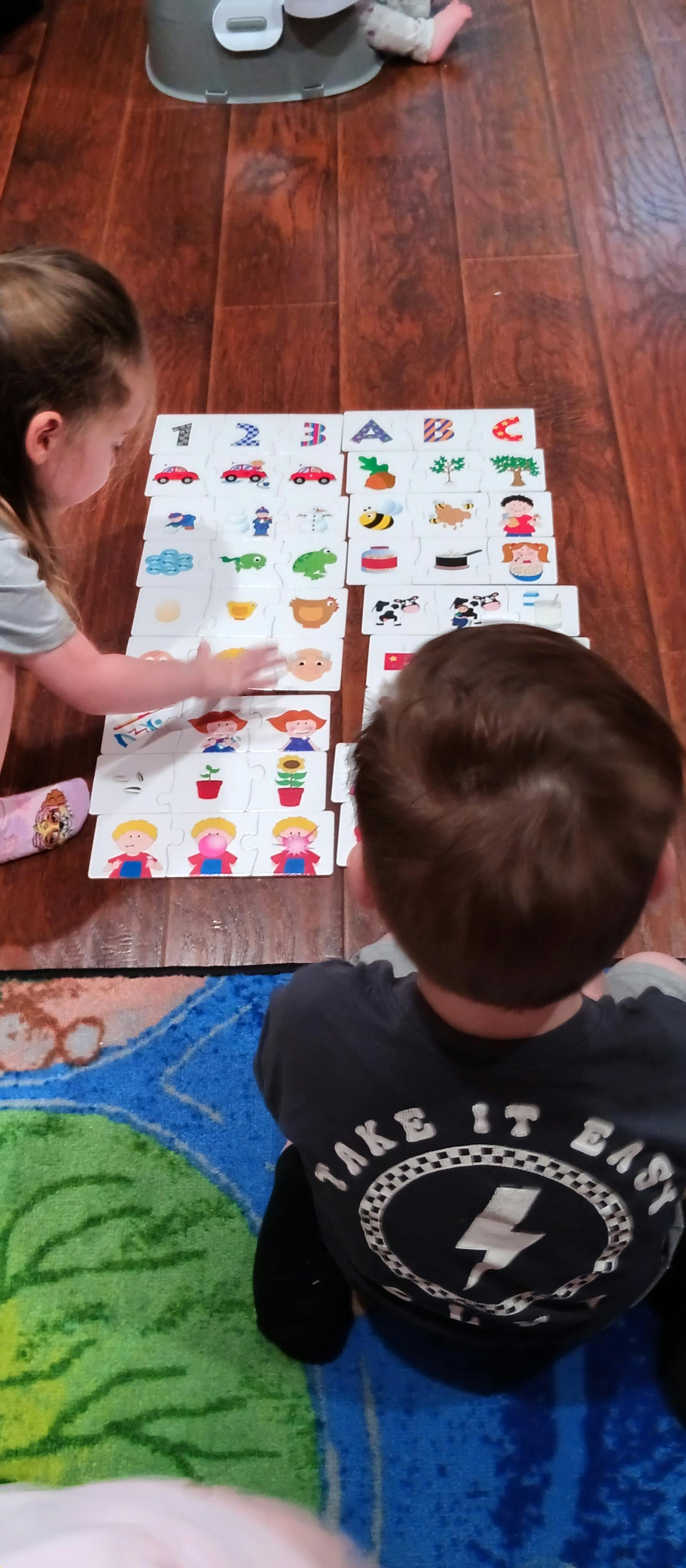 Two children playing with alphabet and number puzzle cards on a wooden floor