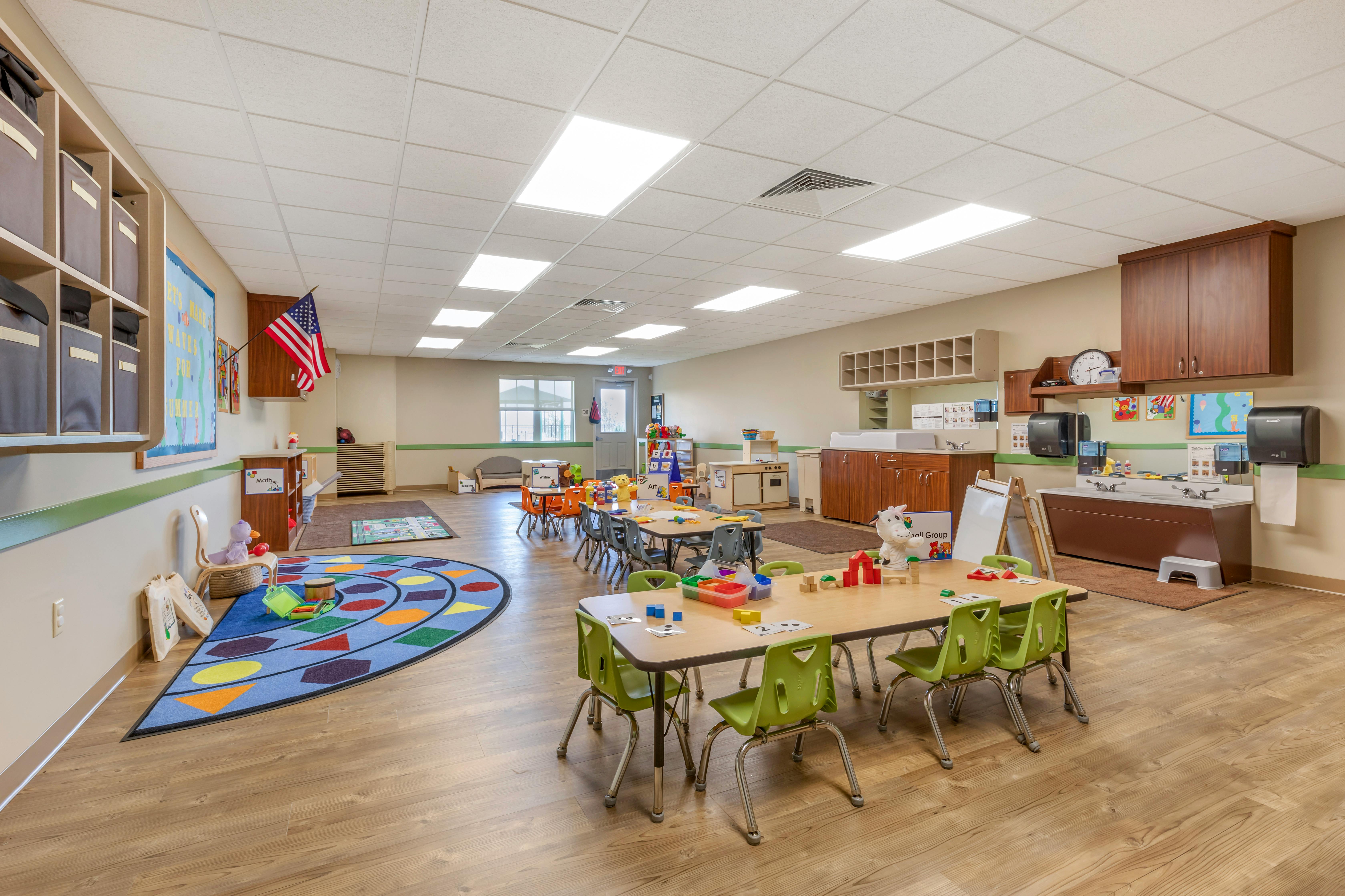 Classroom with tables, chairs, colorful rug, and a sink area