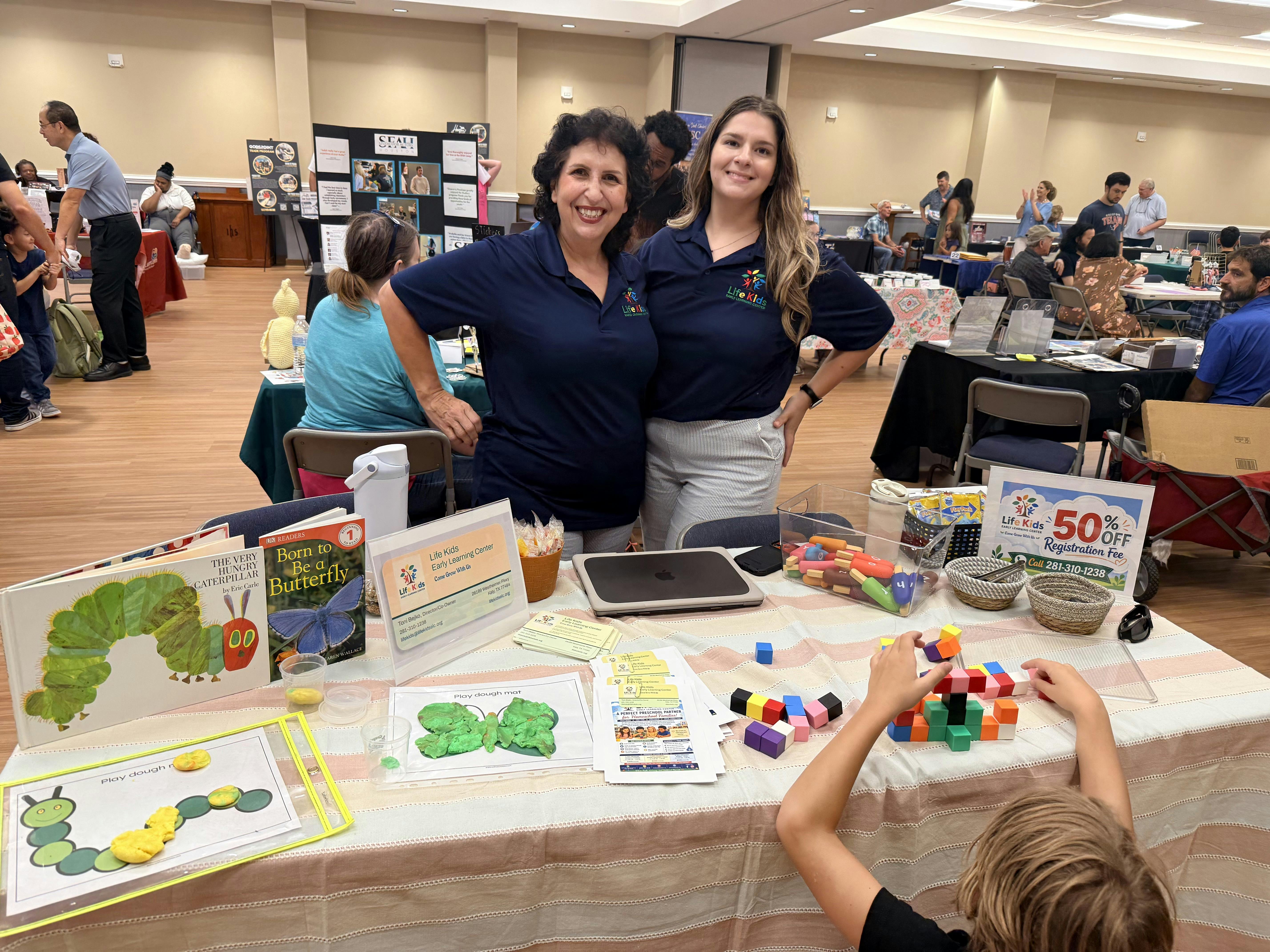 Two adults standing at a Life Kids booth with a child playing with blocks