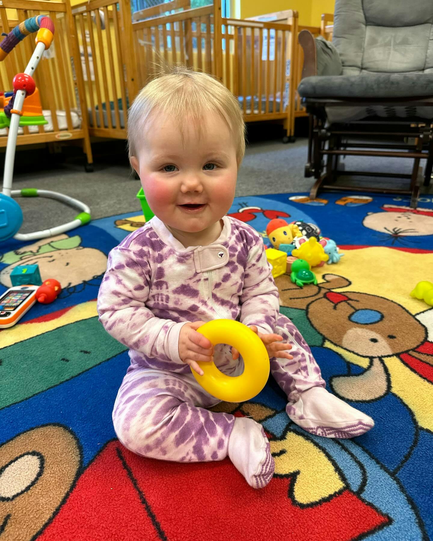 Child sitting on a colorful rug holding a yellow toy ring