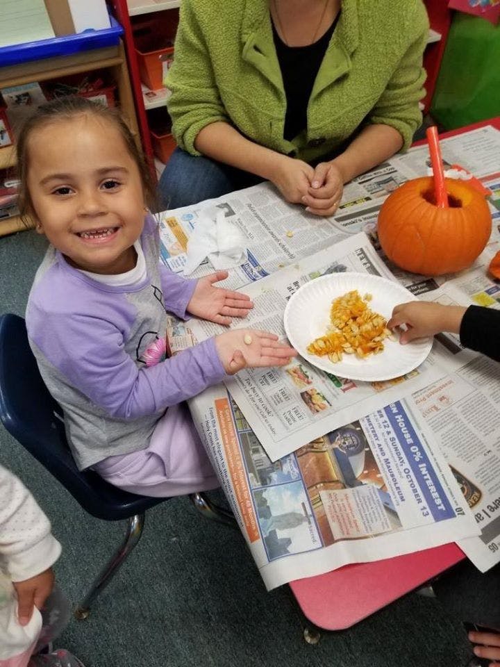 Child at a table with a pumpkin and pumpkin guts on a plate