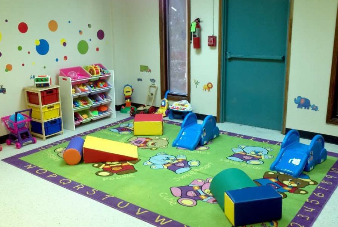 Playroom with a green rug, soft play equipment, and toy shelves