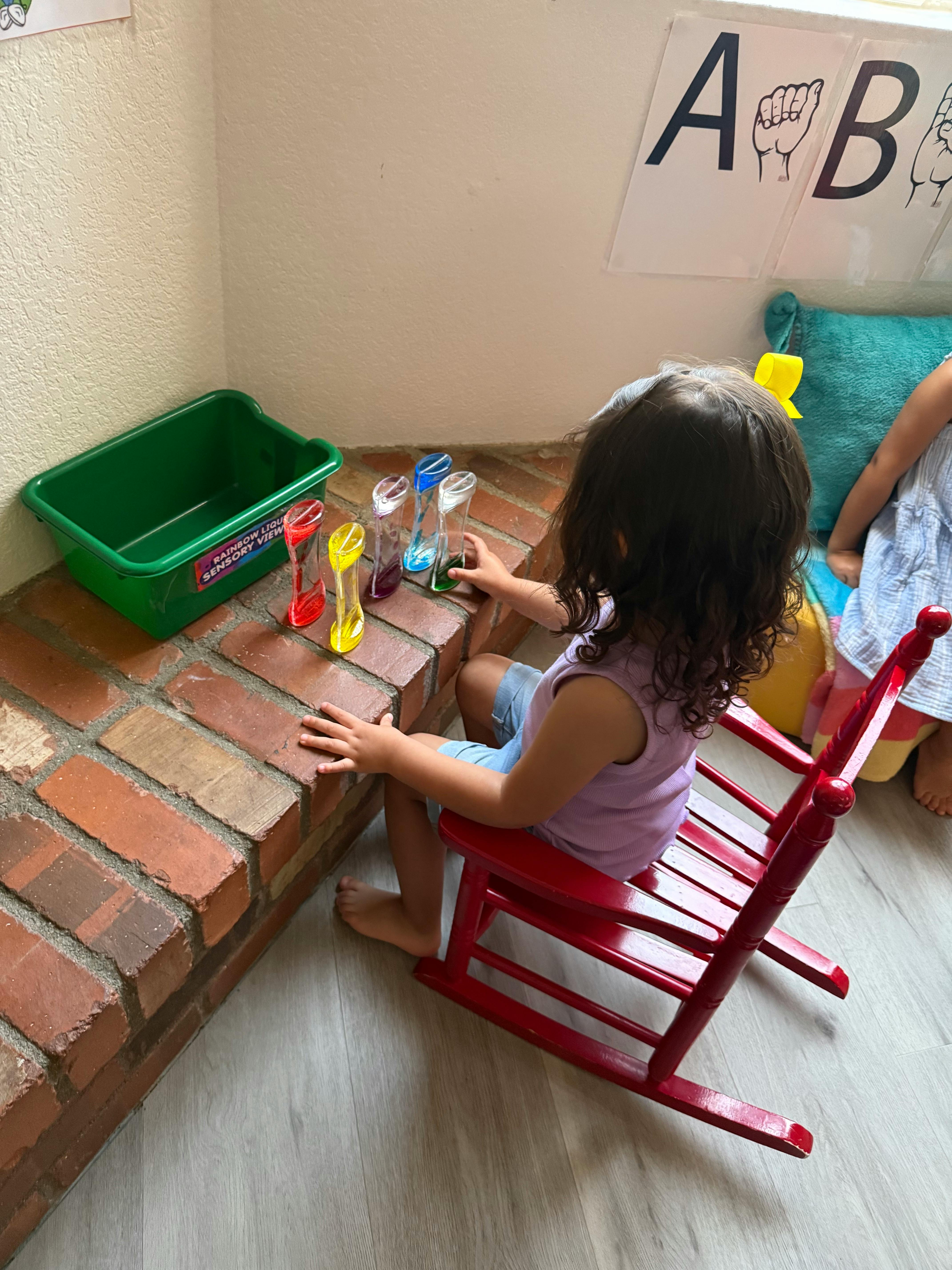 Child sitting in a red rocking chair playing with bottles