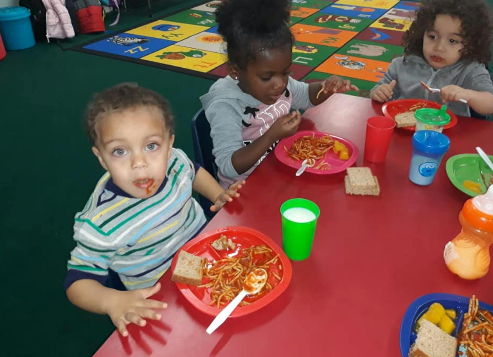 Children eating spaghetti at a red table